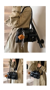 Detail of black PU leather pillow bag featuring front buckle pockets and a teddy bear charm
