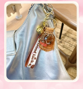 Close-up of miniature soda bottle keychain with golden bell and lucky wrist strap