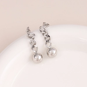 Detail of silver chain earrings with a polished metal ball on a minimalist white tray