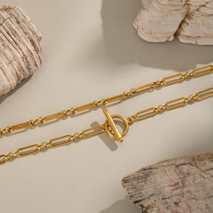 Détail du collier chaîne trombone doré avec fermoir en T sur fond de bois organique naturel