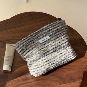 Close-up of black and white tweed cosmetic bag with a simple wish label on a wood table