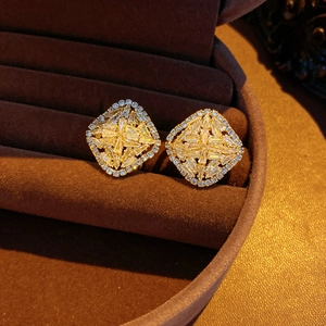 Macro shot of gold geometric diamond earrings with shimmering white zircons on velvet