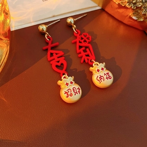 Detail view of red and gold Chinese tassel earrings with lucky symbols on leather surface