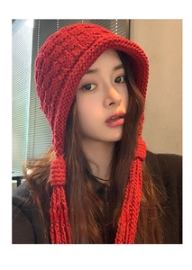 Close-up detail of red chunky knit beanie featuring braided tassels and textured wool