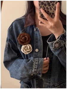 Detail of elegant flocked leather camellia brooches in brown and cream worn by model