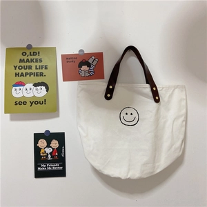 Close-up of white canvas polka dot tote featuring black smiley face and leather handle