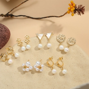 Elegant gold geometric earrings set featuring triangles and pearls on a rustic tray