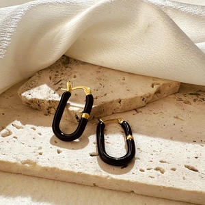 Detail view of U-shaped black and 18K gold plated stainless steel earrings on stone