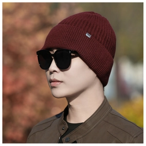Close-up of burgundy knit beanie featuring vertical ribbed texture and a metal logo detail