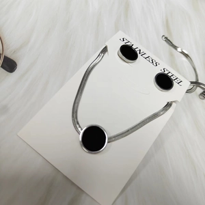 Detailed view of silver stainless steel jewelry set with black round pendants on white fur