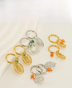 Détail de boucles d'oreilles créoles en acier avec breloques tournesol, œil et perles colorées