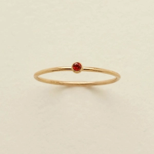 Detailed close-up of a gold S925 ring with a red gemstone on a beige textured background
