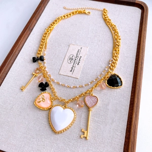 Dettaglio collana vintage multistrato dorata con ciondoli a cuore e chiave su vassoio
