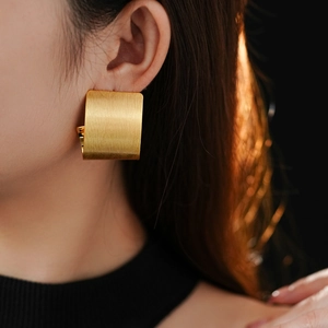Macro detail of matte gold geometric rectangular earrings with brushed metal finish