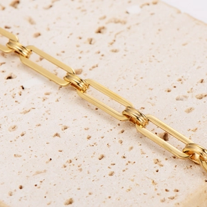 Golden stainless steel paperclip chain bracelet on a beige stone base macro view