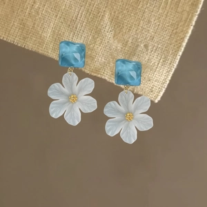 Close-up of elegant acrylic flower drop earrings with translucent blue square studs.