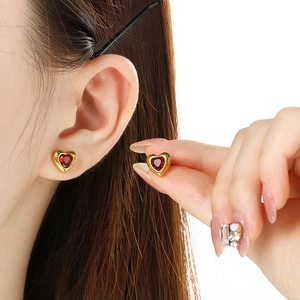 Minimalist gold heart stud earrings set with red rhinestones shown on model ear and fingers