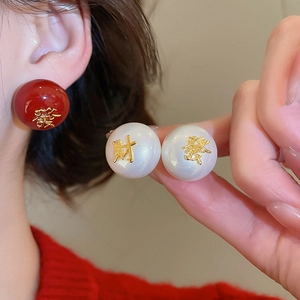 Détail de boucles d'oreilles perles du Nouvel An avec perles rouges et caractères dorés