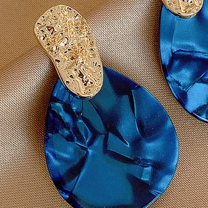 Detail of blue acrylic teardrop earrings with gold metal texture on brown silk fabric
