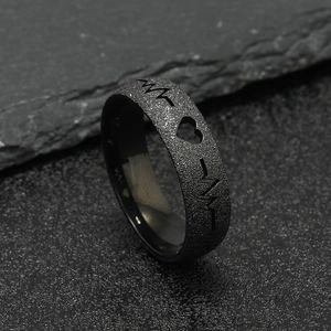 Macro shot of black matte ring with heartbeat EKG cutout on a dark stone background