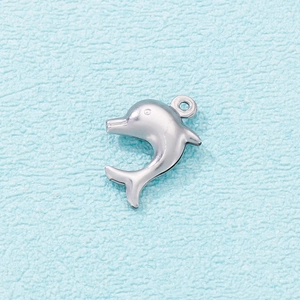 Detailed view of silver stainless steel dolphin pendant on light blue textured fabric