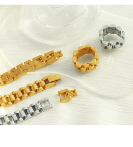 Detailed close-up of gold and silver watchband style chain bracelets and rings on a textured surface