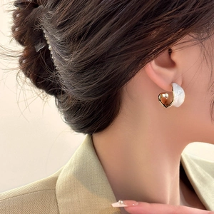 Close-up of a woman wearing gold-plated C-shaped earrings with white enamel finish