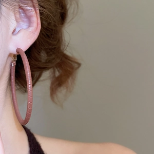 Detailed close-up of oversized hoop earrings wrapped in brown leather with a vintage texture