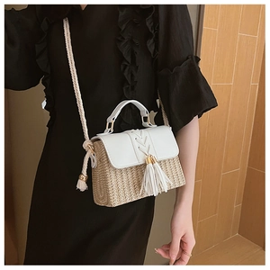 Detail of a straw crossbody bag featuring white leather flap and a woven tassel charm