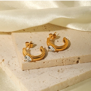 Close-up of golden C-shaped stainless steel earrings with heart-shaped zircon detail