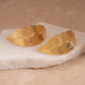 Elegant gold leaf earrings with textured metallic finish on white crystal stone display