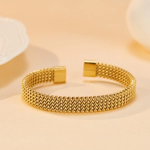 Detail of gold-plated mesh texture and square end caps on an open stainless steel cuff