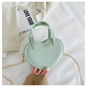 Detail of mint green heart-shaped jelly bag with gold chain strap on soft white fabric