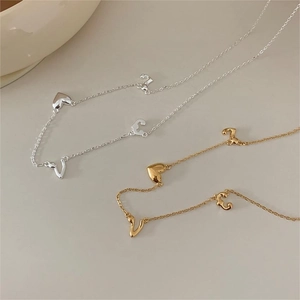 Close-up of minimalist 925 silver and gold LOVE heart necklaces on cream surface