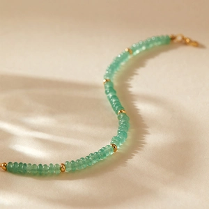 Detail eines grünen Perlenarmbands mit Goldakzenten und edlen Lichtschatten