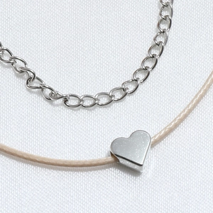 Detailed macro shot of a dual-layer necklace with a silver heart pendant and woven rope cord