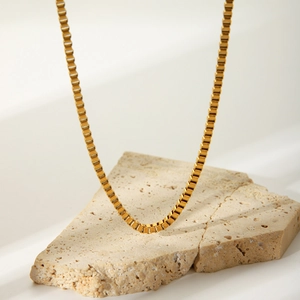 Polished gold plated stainless steel box chain necklace displayed on a textured stone slab