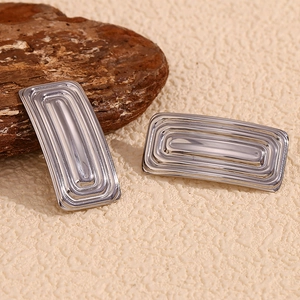 Macro detail of silver rectangular stud earrings with concentric grooved texture on wood