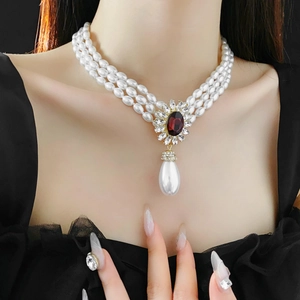 Detailed view of triple-layer pearl necklace with red gemstone and teardrop pearl pendant