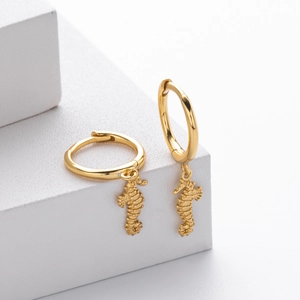 Macro detail of golden seahorse pendant earrings with fine textured metallic finish