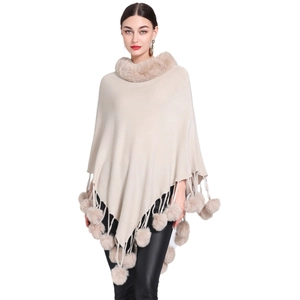 Beige knitted poncho cloak with faux fur collar and tassel pom-poms for winter