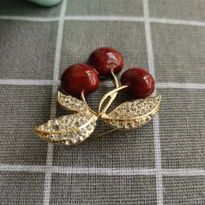 Détail de la broche cerise en émail rouge avec feuilles dorées et cristaux sur tissu