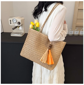 Close-up of woven straw tote bag with vibrant orange and brown tassel decorations