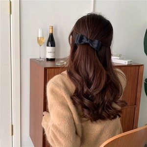 Detail of black fabric bow hair clip worn by a model in a cozy, aesthetic home setting