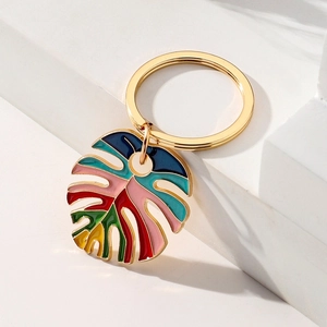 Golden keychain with colorful monstera leaf pendant on minimalist white background