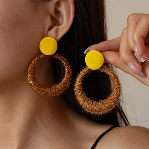 Detail of model wearing gold-brown flocked circular hoop earrings with yellow studs