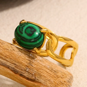 Macro detail of 18K gold-plated ring with oval malachite stone on rustic wood branch