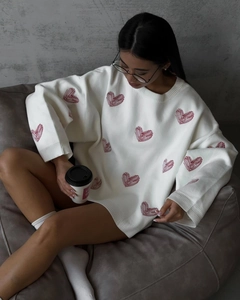 Detail of red heart embroidery on white oversized knit sweater with casual round neck
