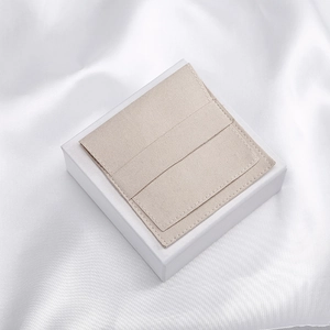 Detail view of a beige microfiber jewelry pouch on a white square gift box with silk background