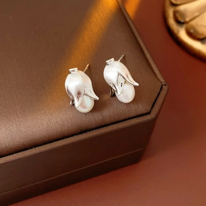 Detailed close-up of a silver flower bud earring with a pearl on a brown jewelry box